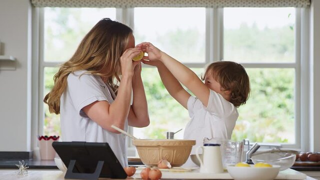 Mother and son in pyjamas making funny faces with lemons as they bake in kitchen at home together - shot in slow motion