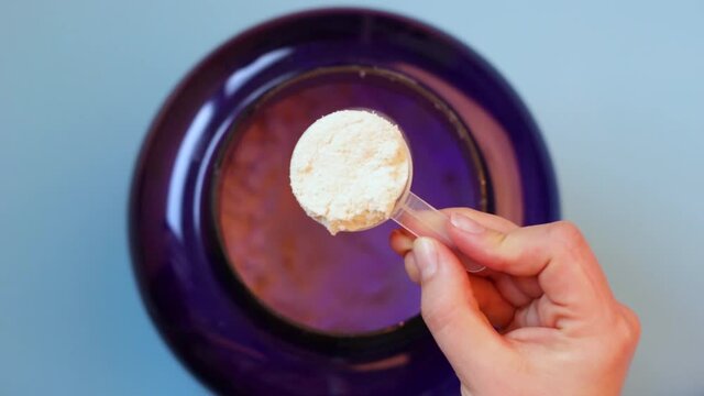 Scoop with protein in female hand top view, blue background