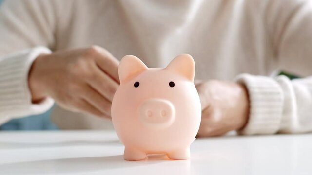 Closeup man hand put coin money to piggy bank, saving and deposit money concept