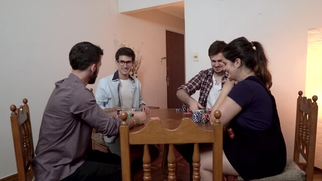 Friends playing poker sitting on a wooden circular table at home