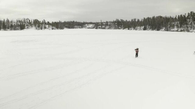 Adult man in large fur hat, walks and plays in traditional snowshoes on frozen lake with his pet dogs in northern Canada.