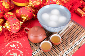 A bowl of glutinous rice balls, tea and red envelopes on the background of festivity