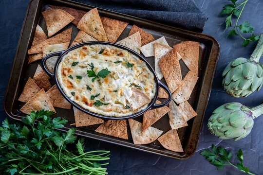Top down view of a baking sheet filled with pita triangles and a hot artichoke dip in the middle.