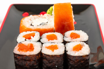 fresh appetizing philadelphia rolls with salmon and soft cheese in black red plates on a white background