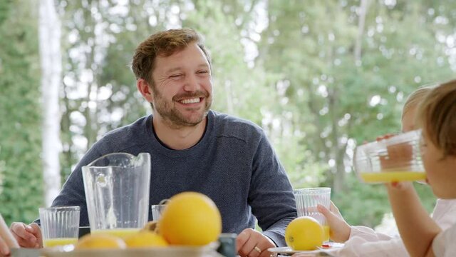 Family wearing pyjamas sit around table enjoying pancake breakfast together - shot in slow motion