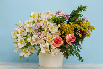 Arreglo floral con diferentes tipos de flores sobre una mesa y un fondo de color azul. Concepto decoración para eventos sociales
