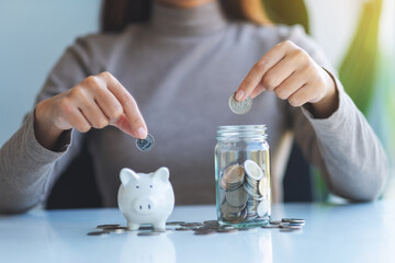 Closeup image of a woman putting coin into piggy bank and a glass jar for saving money concept