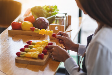 Closeup image of a beautiful female chef holding fresh mixed fruits on skewers in a wooden plate