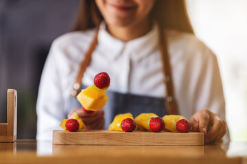 Closeup image of a beautiful female chef holding fresh mixed fruits on skewers in a wooden plate