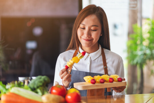 Closeup image of a beautiful female chef holding fresh mixed fruits on skewers in a wooden plate