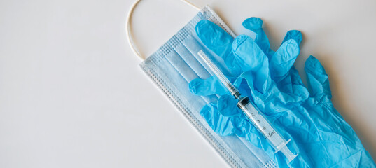 Medical mask, syringe, blue latex gloves on white background with copy space, close-up. Concept of vaccination of the population.