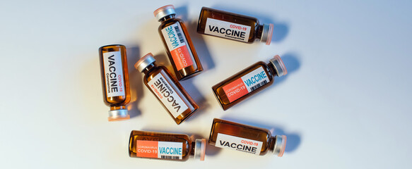Vials of different coronavirus vaccine lie randomly on white background, close-up. Covid-19 banner with copy space. Completion of development of antiviral drug, mass vaccination of population.