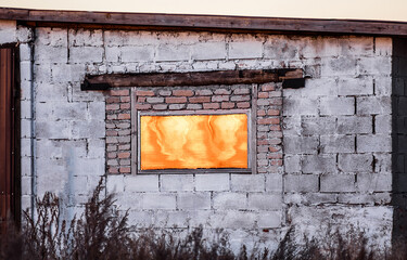 Brick wall of a rural house with a window covered with a sheet of metal reflecting the golden sunset light of the sun