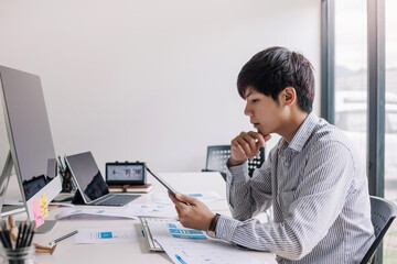Asian business man think and watch smartphones and laptops on their desks in the office.