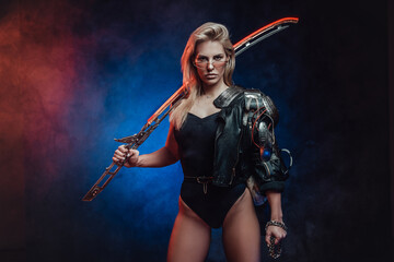 Fototapeta na wymiar Dangerous and at the same time beautiful female fighter from the future poses in dark background holding her blade on her shoulder.