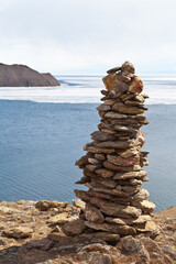 Baikal Lake in the spring. A high stone pyramid on top of a cliff - local traditions, rituals, superstitions. Top view of the ice drift on a sunny April day. Travel and outdoor activities concept