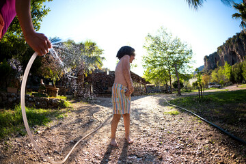 Boy splashed with water from a hose in the courtyard of the house on a hot sunny day.