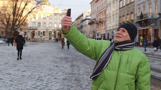 Senior man grandfather tourists traveling walking taking selfie pictures, making online video call in European winter city Lviv, Ukraine. Active life after retirement. Christmas holidays tour vacation