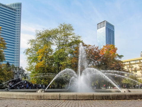 Fountain near Monument to Janusz Korczak in Swietokrzyski Park in Warsaw, Poland. Water sprays from the old stone pool against the modern skyscrapers on an autumn sunny day, background with copy space