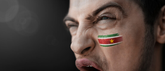 A screaming man with the image of the Suriname national flag on his face