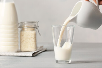 Pouring of rice milk from jug into glass on table