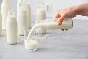 Woman pouring rice milk from bottle into glass on table