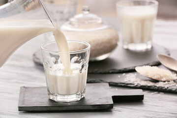 Pouring of rice milk from jug into glass on table