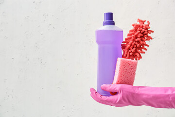 Hand in rubber glove with cleaning supplies on light background