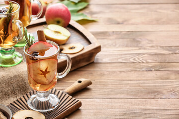 Tasty drink with spices and apple slices in cups on wooden background