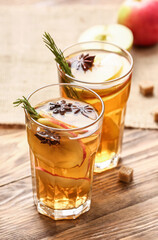 Tasty drink with spices and apple slices in glasses on wooden background