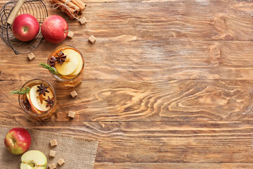 Tasty drink with spices and apple slices in glasses on wooden background