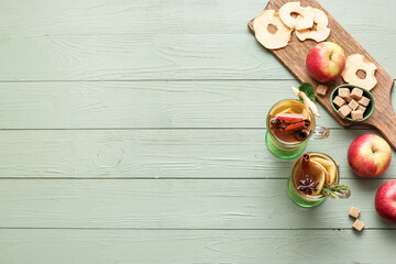 Tasty drink with spices and apple slices in cups on color wooden background