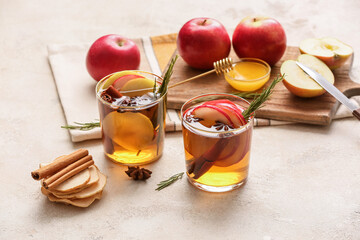 Tasty drink with spices and apple slices in glasses on light background