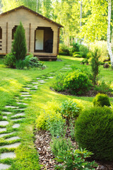stone pathway in summer garden with beautiful wooden house on background. Landspace design with conifers and shrubs