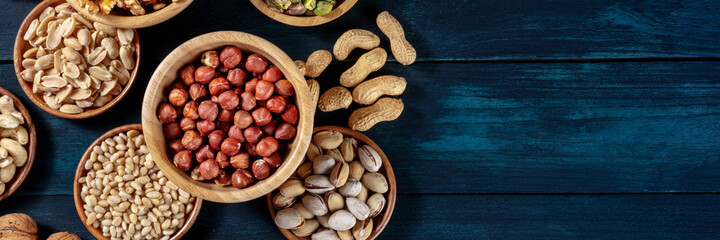 Nuts panoramic banner with a place for text. Various nuts in wooden bowls on a dark blue background