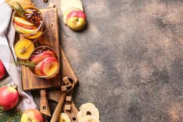 Tasty drink with spices and apple slices in glasses on grunge background