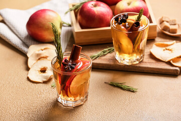Tasty drink with spices and apple slices in glasses on color background