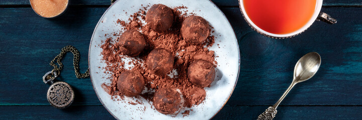Chocolate truffles and tea panorama on a dark blue wooden background