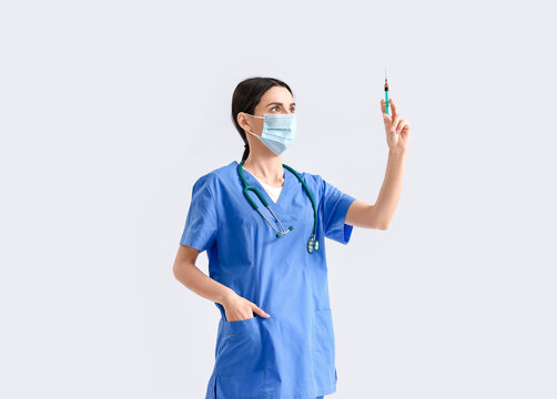 Portrait of female doctor with syringe on light background