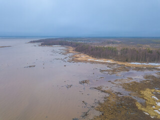 White Sea coast with stony shores covered by green pine trees and snow spots under cold sky. Drone aerial view. Kemsky District, Karelia region, Russia.