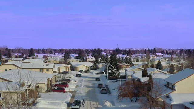 arial panout over blue sky snow covered cars vans streets sidewalks at sidestreet of an Edmonton Alberta subarb of middle to upper class closeup of low rised dettached homes that are paid off mortgage