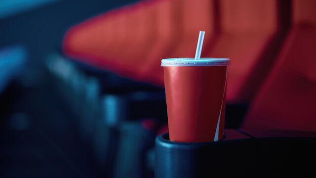 Selective focus on empty disposal cup of soda with red cinema seats in the background