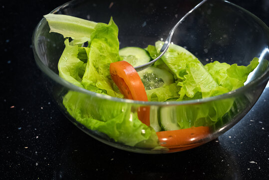 Close up of dlass bowl with green calad and tomato slices. Dieting and healthy eating concept