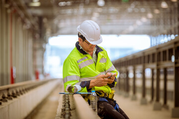 Engineer railway under inspection and checking construction process train and railroad station .Engineer wearing safety uniform and helmet by holding document in work.