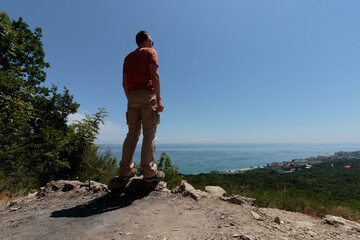 man standing and looking at the sea coast from the top of a hill