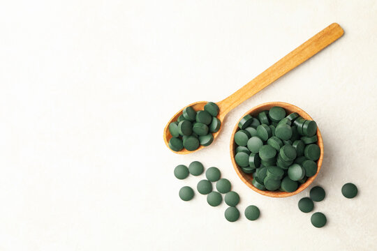 Wooden bowl and spoon with spirulina pills on white textured background