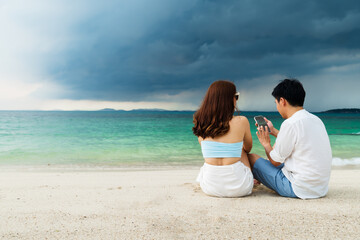 couple using smartphone on the sea beach at Koh MunNork Island, Rayong, Thailand