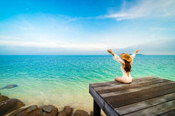 happy woman sitting on a wooden bridge with arm raised in the sea at Koh MunNork Island, Rayong, Thailand
