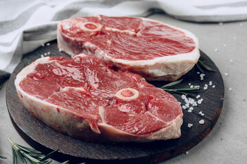 Raw rib-eye beef steak on wooden cutting board on gray background