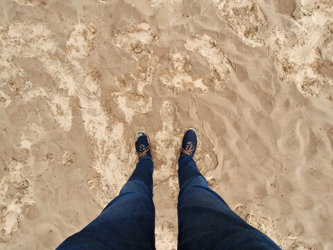 Selfie of foot and legs with casual shoes and jeans on a wet sand seen from above